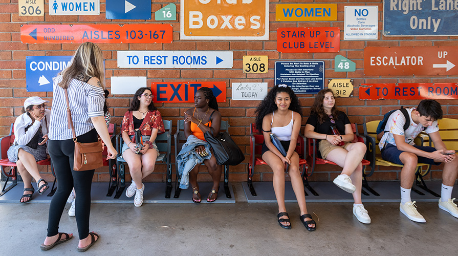 Students attend Dodgers game, backed by brick wall covered in various metal signs