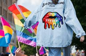 Parade location featuring LGBTQ flats, a person with a denim jacket with a patch on it walks away from the camera.