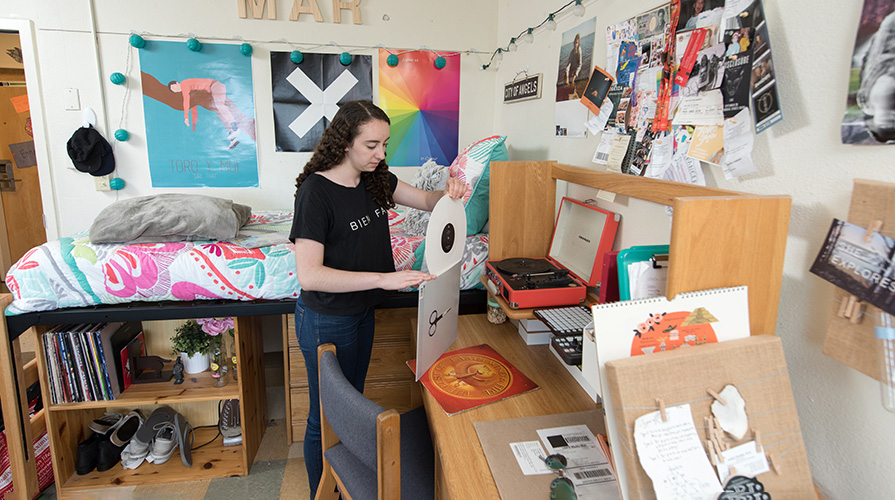 Student in residence hall places vinyl record back into its sleeve, in front of their raised bed and band posters.