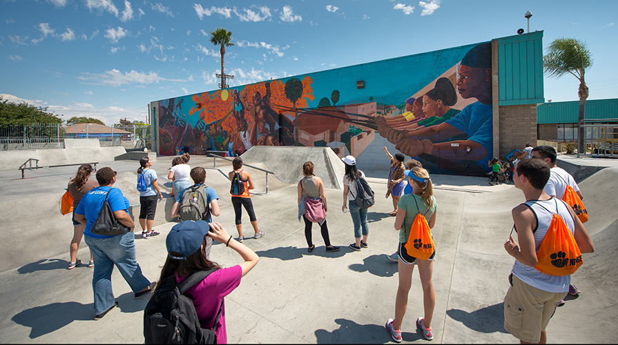 Students look towards where a faculty member is pointing, towards a mural with people of color featured