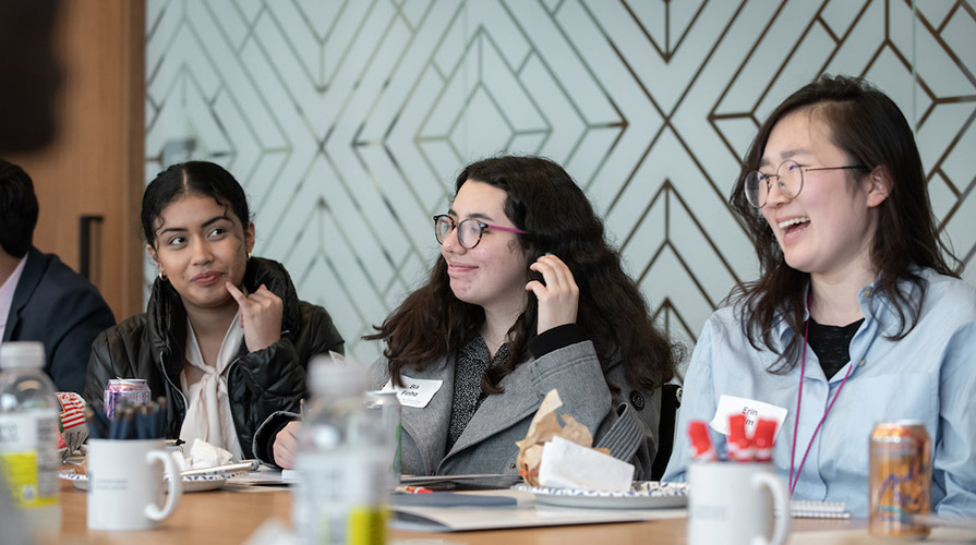 Three students sit at a large table in an office laughing