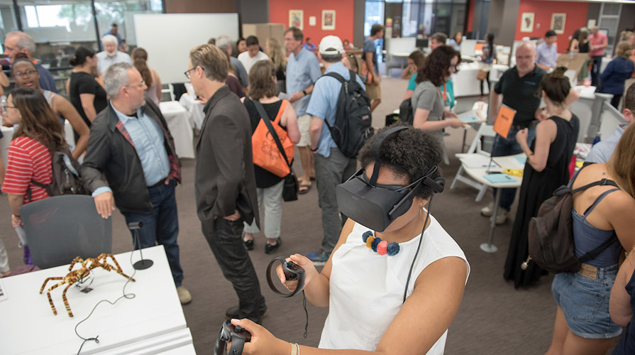 One student uses a VR headset while students and professors chat in the background at Oxy's Academic Fair