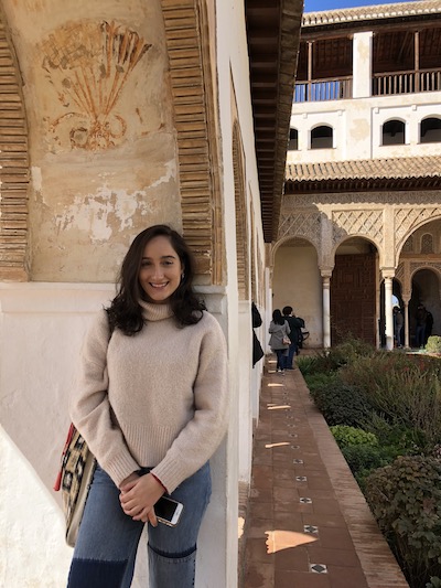picture of Emma leaning on an arch in some sort of European-looking courtyard or. country 