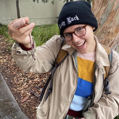 A young person holds something unidentifiable up to the camera, smiling widely.