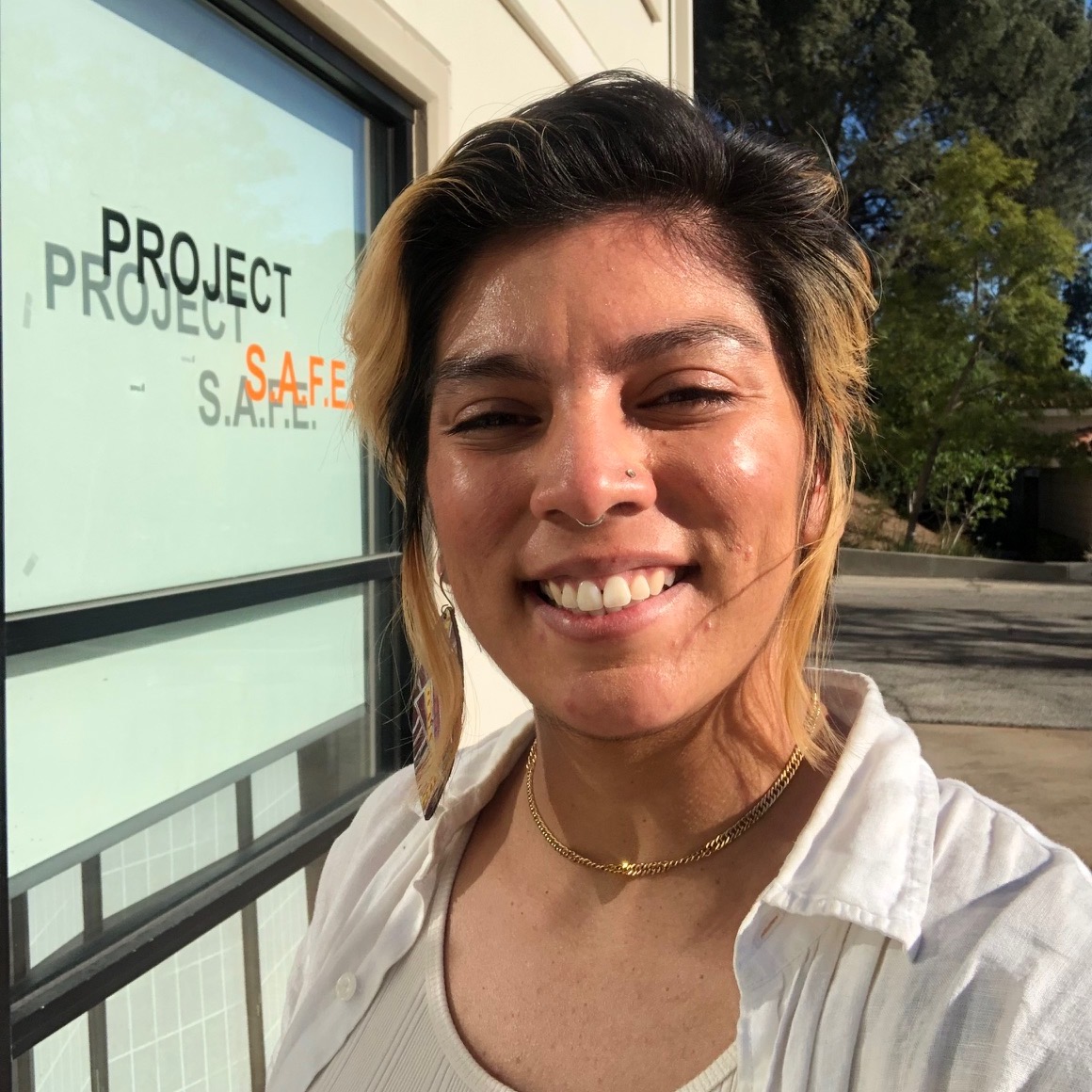 A person smiles at the camera in front of the Project SAFE office.