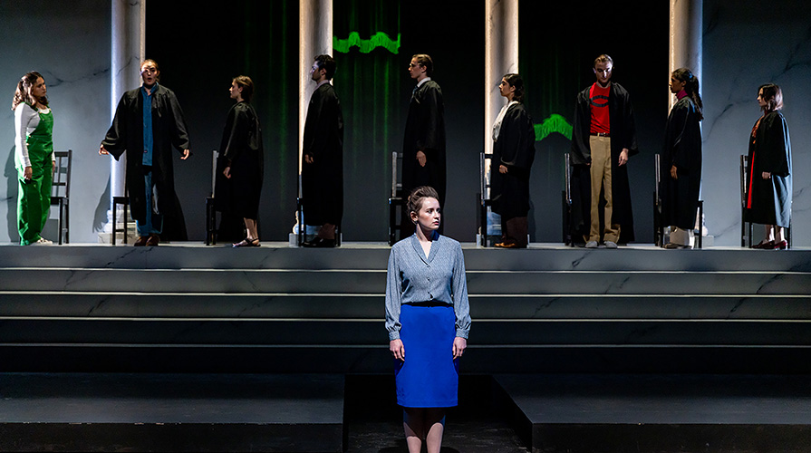 woman standing on stage with a simulated court of supreme court judges behind her