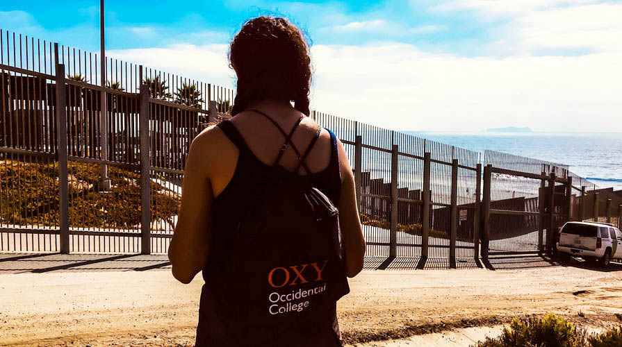 Oxy student stands by a border wall