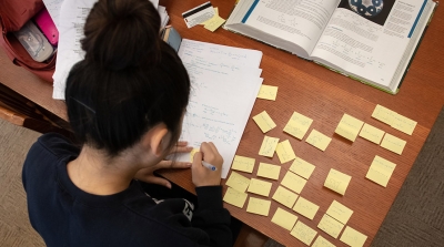 A student studies for final exams at a desk covered with papers and sticky notes