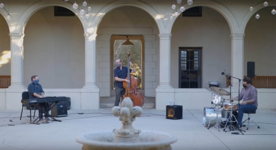A jazz trio of piano, bass, and drums performing in the Booth Hall courtyard