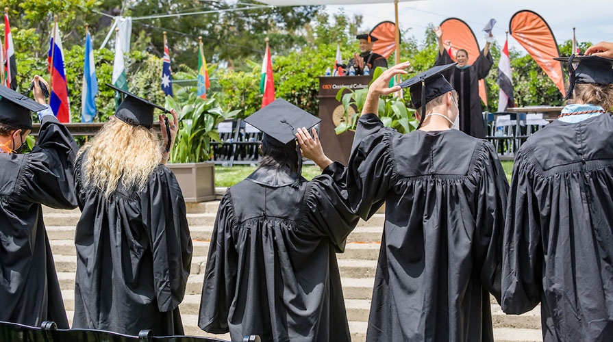 Five graduates from the back, moving their cap tassels to the back