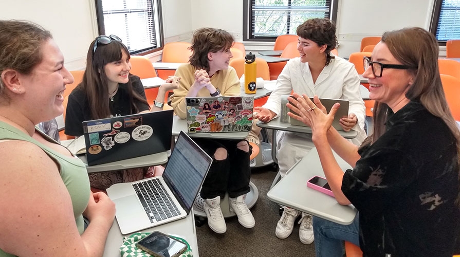 A group of four students and a professor in a semi-circle, talking and laughing