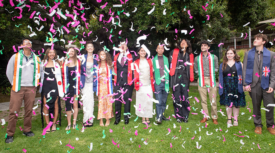 a standing group of Occidental College international students at their graduation with confetti in the air