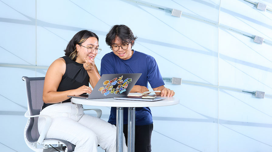Two Occidental students looking at a laptop screen together, smiling