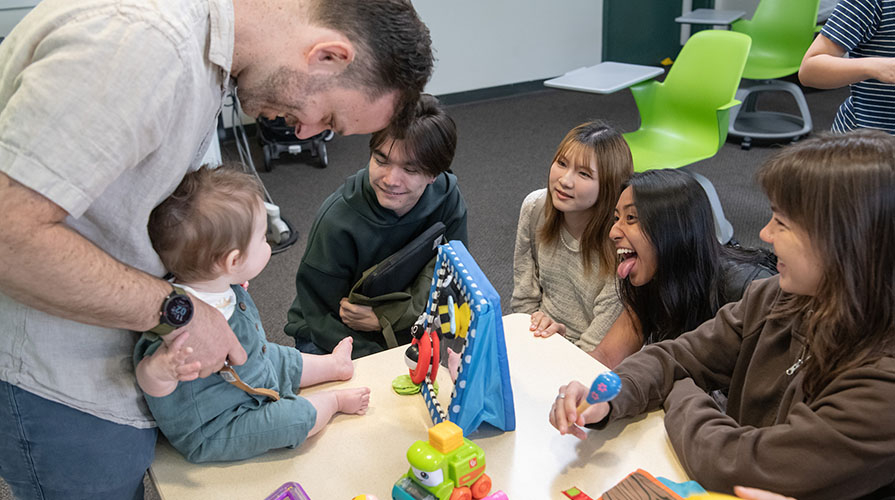 Occidental College professor Nicholas Grebe and his baby interacting with psychology students in the classroom