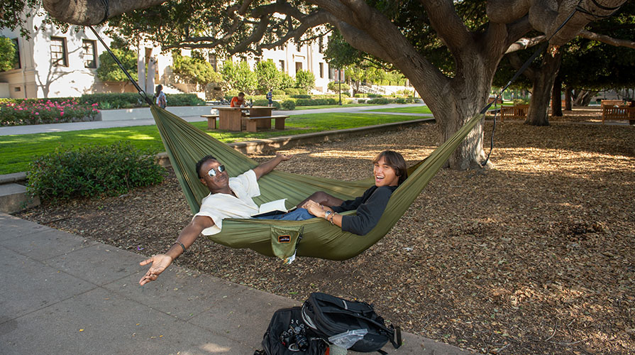 Two Occidental Students sitting in a hammock with their arms outstretched