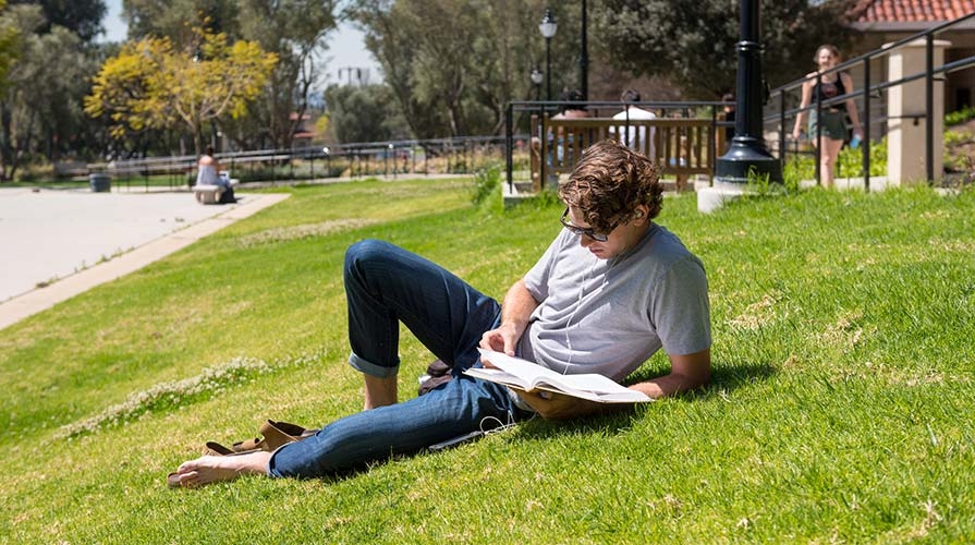 Student lounging on the campus lawn reading a book