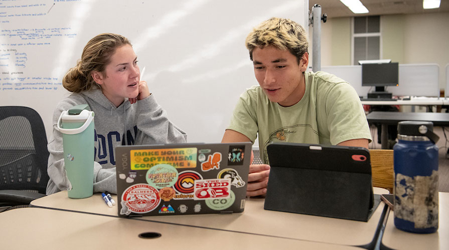 Two Occidental College students talking together with their laptops in the library