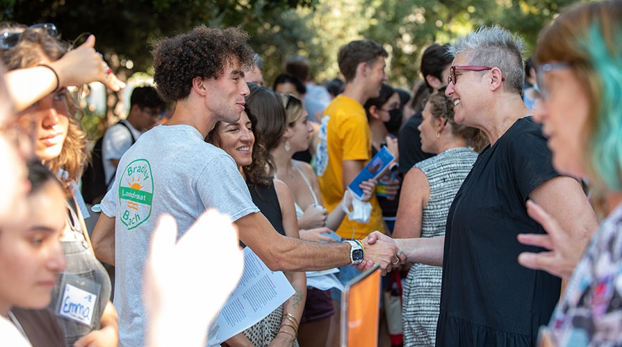 A student and a professor in a group, shaking hands