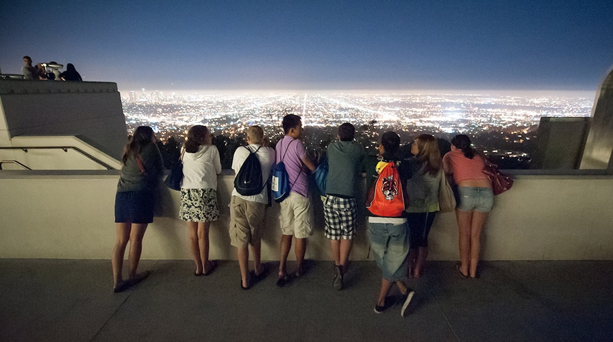 Students look over the lights of Los Angeles at night from the Griffith Park Observatory