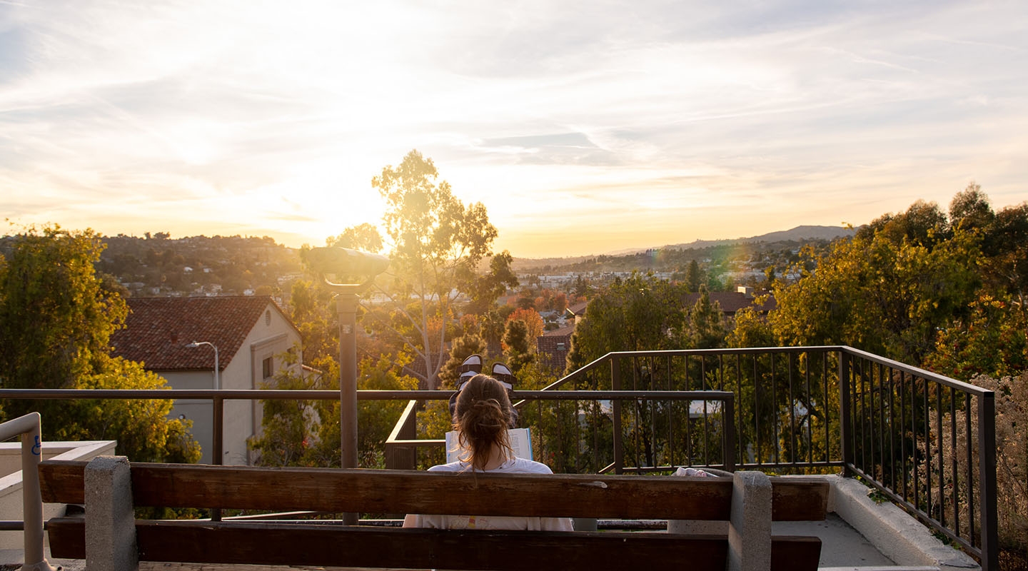 an Occidental student reading a book on a bench on campus as the sun sets