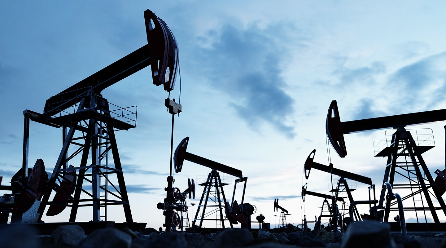 a series of silhouetted oil rigs against a blue, cloudy sky