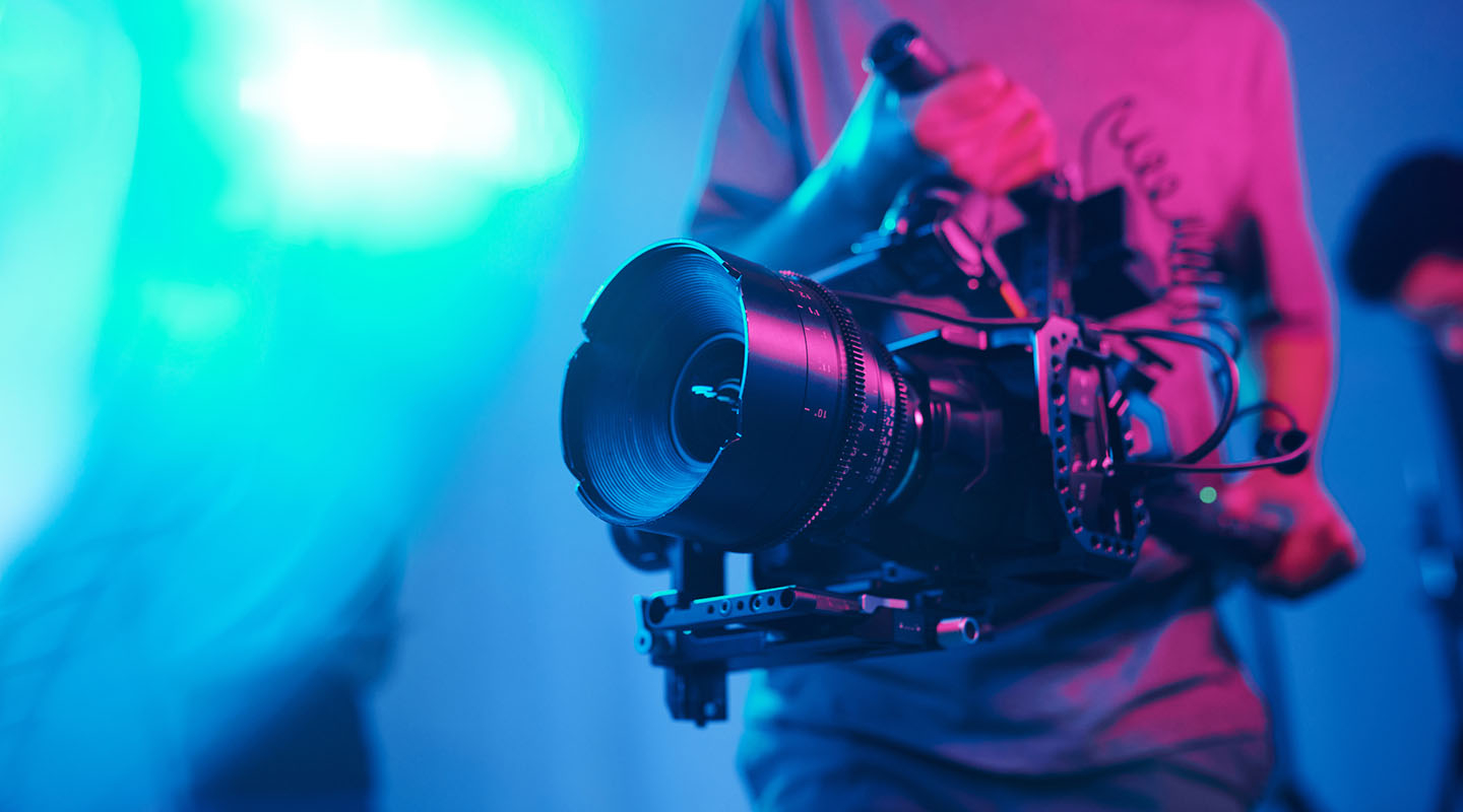 a cameraman holding a film camera with a colored background