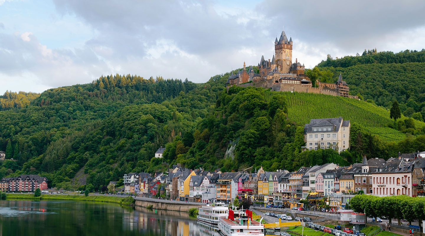 a beautiful hillside topped with a European castle next to a river