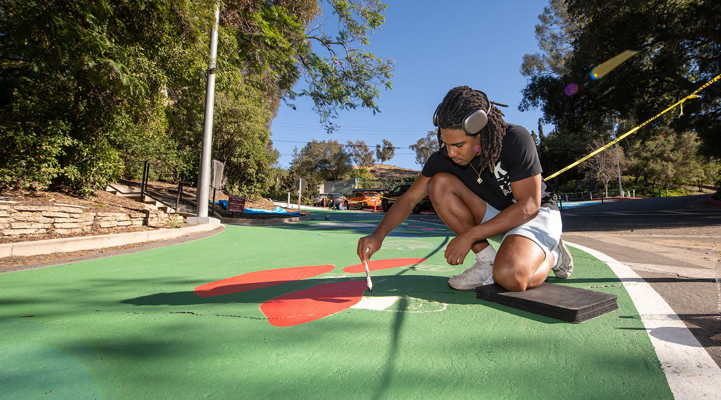 An Occidental College student paints a mural on a road on upper campus