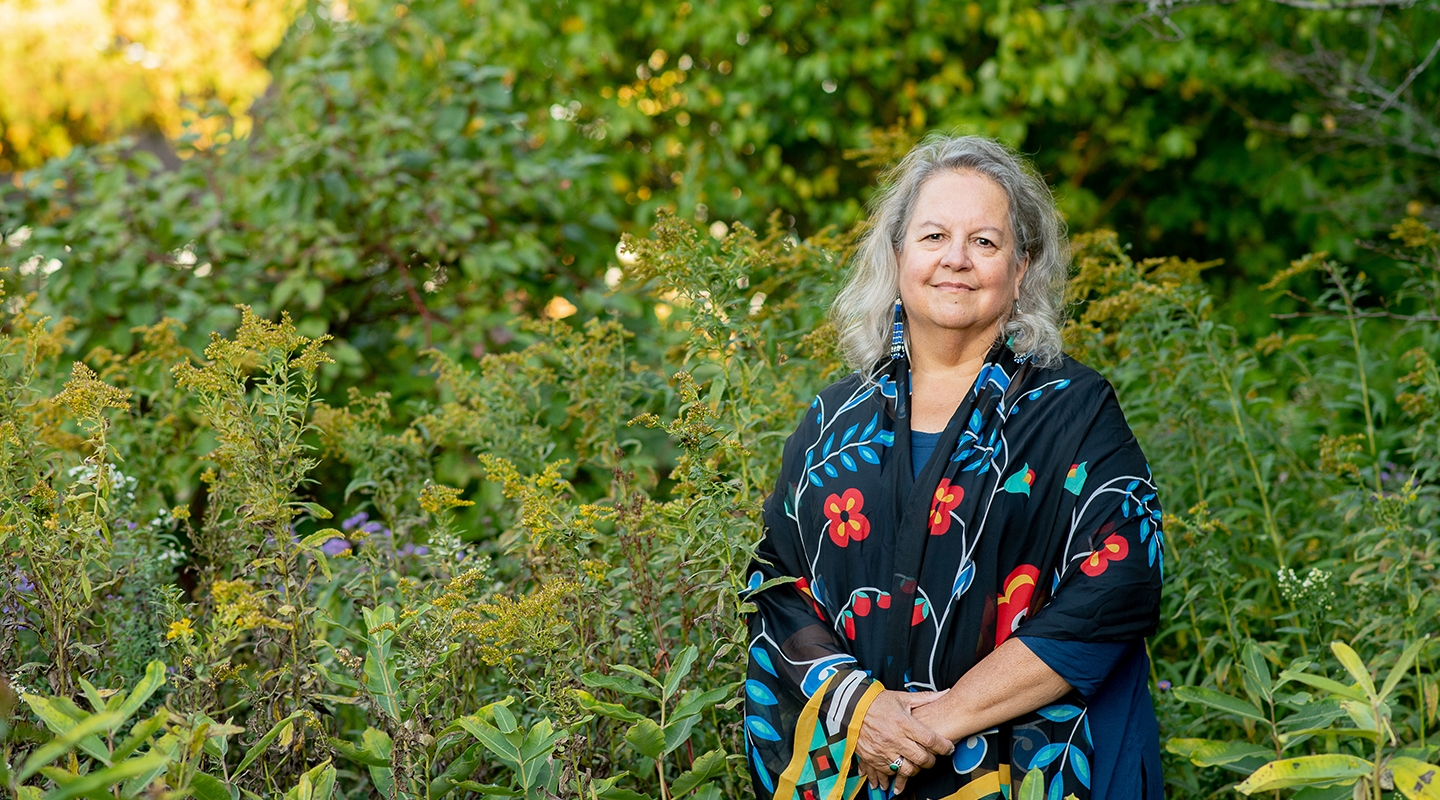 Robin Wall Kimmerer photographed outdoors in front of a green setting with wildflowers