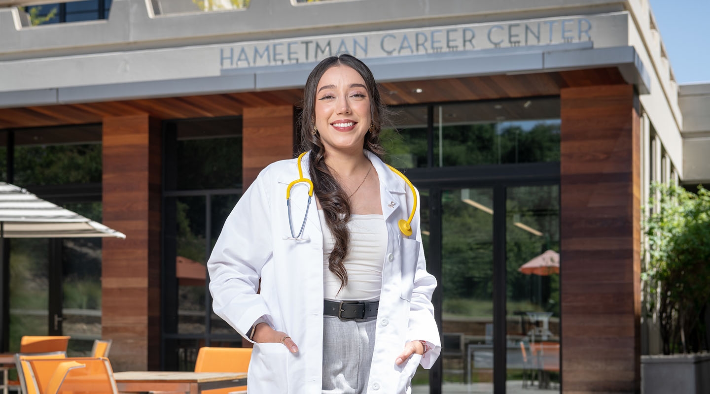 A young Oxy alumna stands outside the HCC with a medical coat and stethiscope
