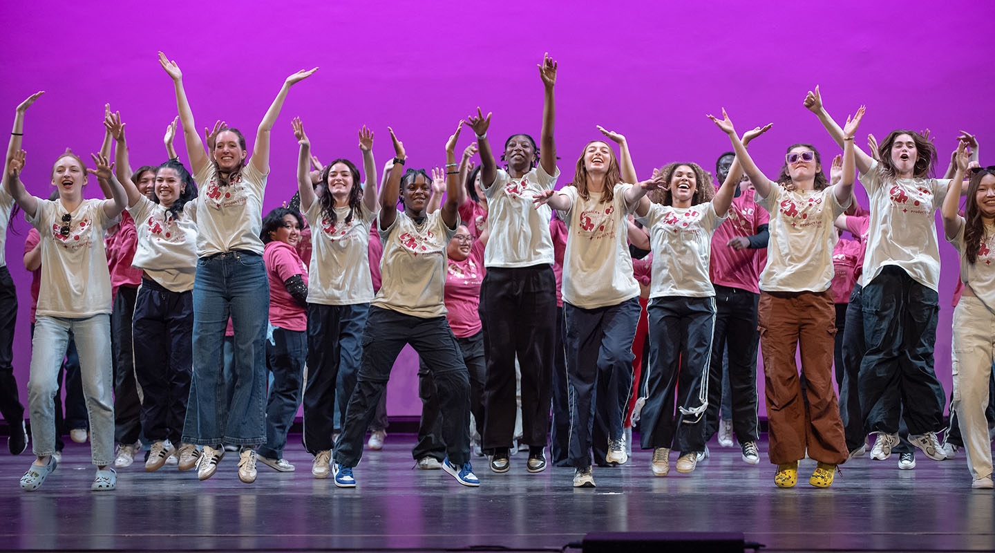Oxy students on stage, arms up and smiling as they perform in Dance Pro