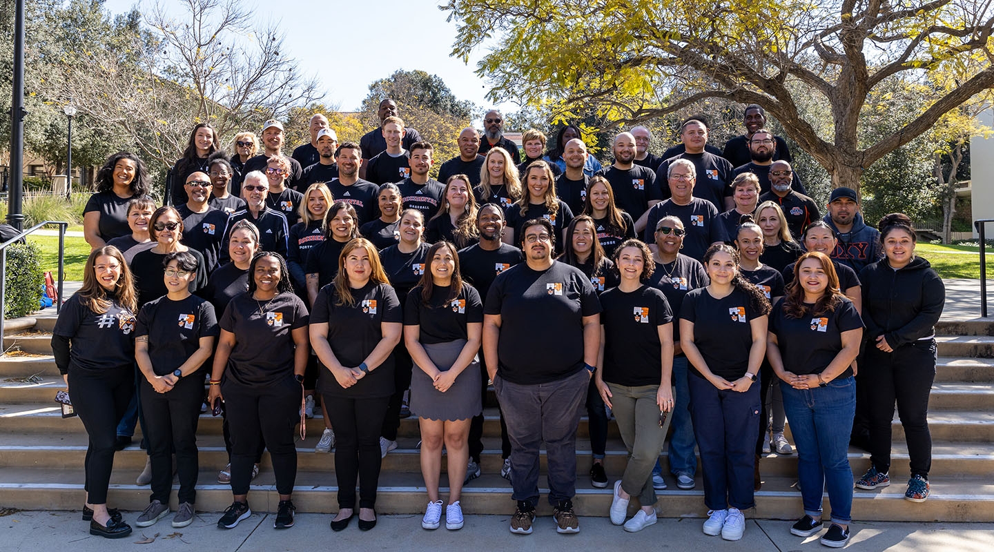 A large group of Student Affairs staffers standing on the steps on campus in black tshirts