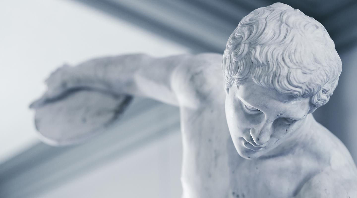 An ancient Greek or Roman sculpture of a man with his arm stretching back to throw a discus, representing the Classical Studies program at Occidental College (Oxy).