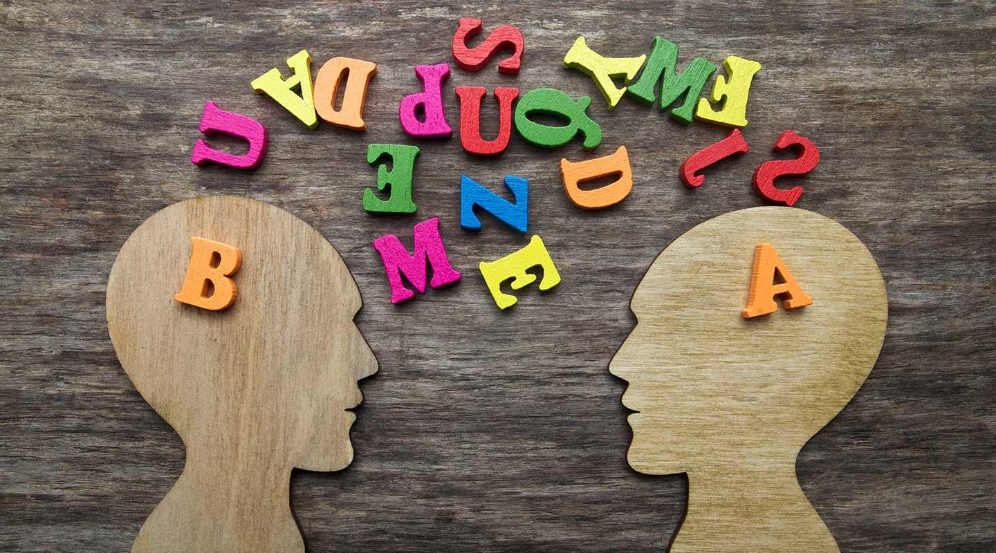 two wooden head cutouts and colored jumbled letters representing different individuals attempting to communicate