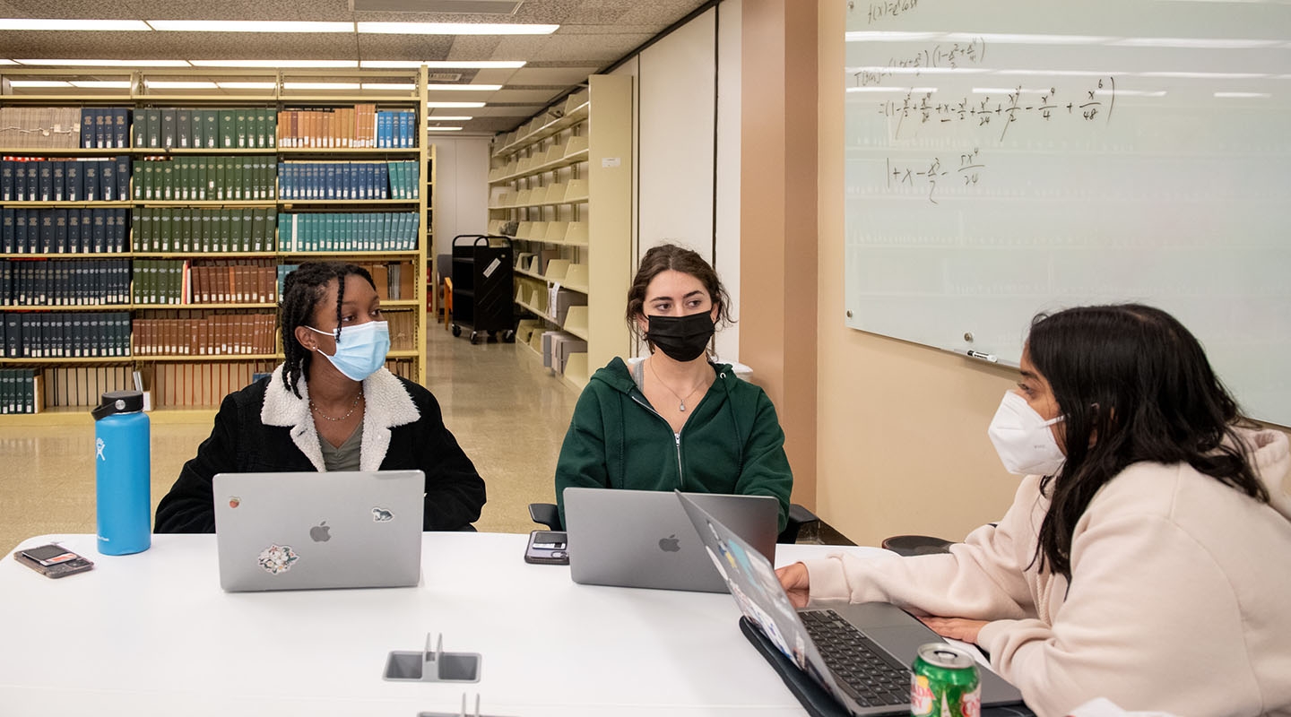 students studying together in the library, wearing masks