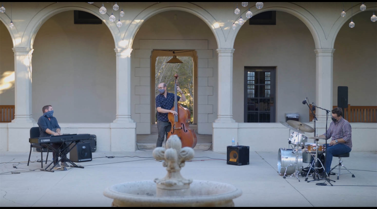 A jazz trio of piano, bass, and drums performing in the Booth Hall courtyard