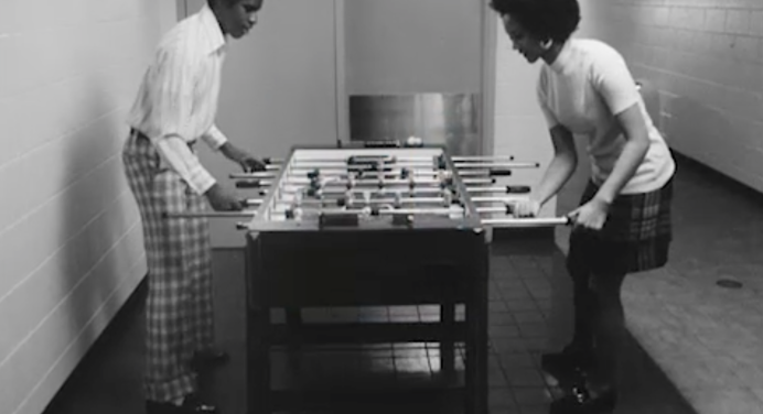 Black and white photograph of two Black people playing foosball 