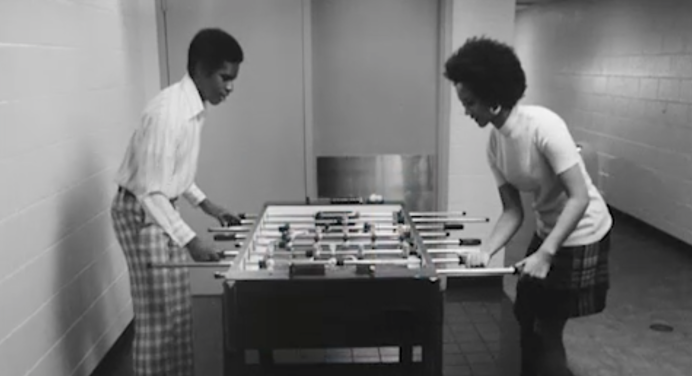 Black and white photograph of two Black people playing foosball 