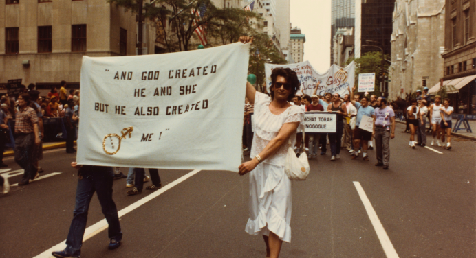 Archival image of Sylvia Rivera walking in a protest holding a large banner 