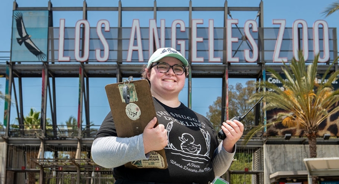 Oxy student intern with a clipboard in front of the Los Angeles Zoo sign