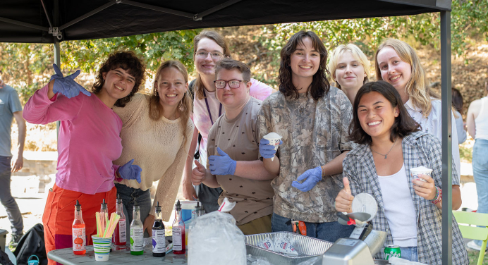 A happy group of Occidental College students posing together at a snow cone assembly table