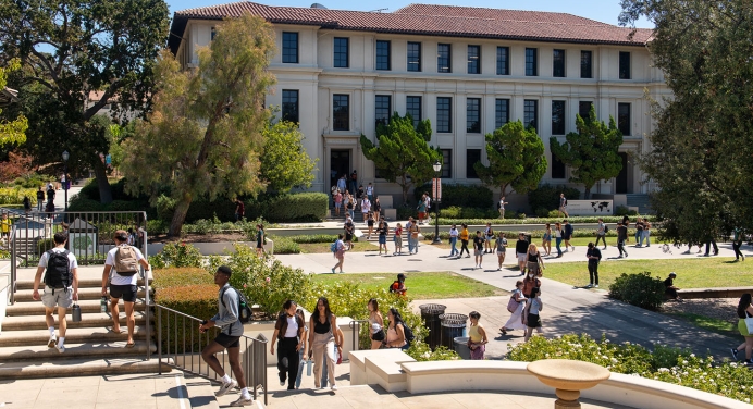 A view of Occidental College students on campus, entering Johnson Student Center and walking up steps with Fowler Hall in the background.