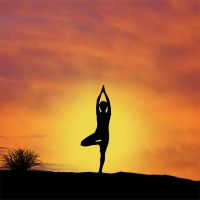 Silhouette of a person doing a yoga pose in front of a yellow sunset.