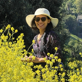 Tuyetdong Phan-Yamada headshot in a field of flowers wearing a hat