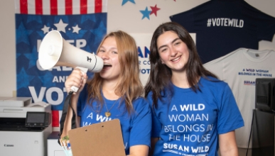 Two female Occidental students stand together with clipboards, a megaphone and blue campaign tshirts
