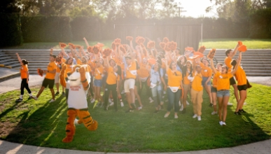 A crowd of Occidental College O-Team orientation leaders, cheering in a green field with Oswald in front