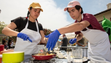 Two Occidental College students in aprons, cooking together over a stove top