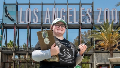 Oxy student intern with a clipboard in front of the Los Angeles Zoo sign