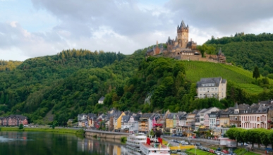 a beautiful hillside topped with a European castle next to a river