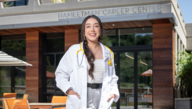 A young Oxy alumna stands outside the HCC with a medical coat and stethiscope